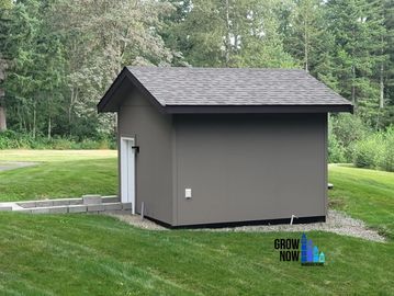 Small gray shed in a grassy backyard.
