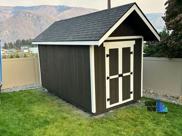Black and white garden shed on a lawn with mountains in the background.