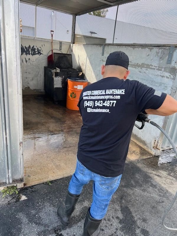 Worker power washing a commercial outdoor area wearing maintenance company T-shirt.