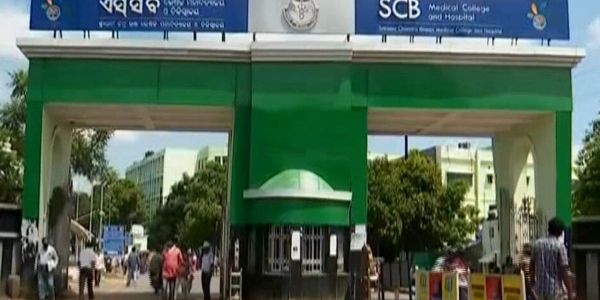 Entrance gate of SCB Medical College and Hospital with people walking by.