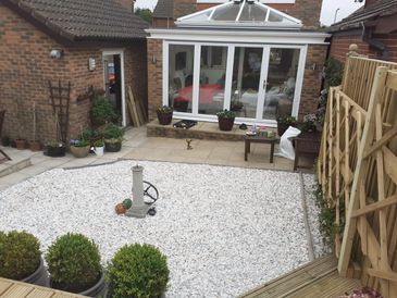 A backyard garden with white gravel, potted plants, and a glass conservatory.
