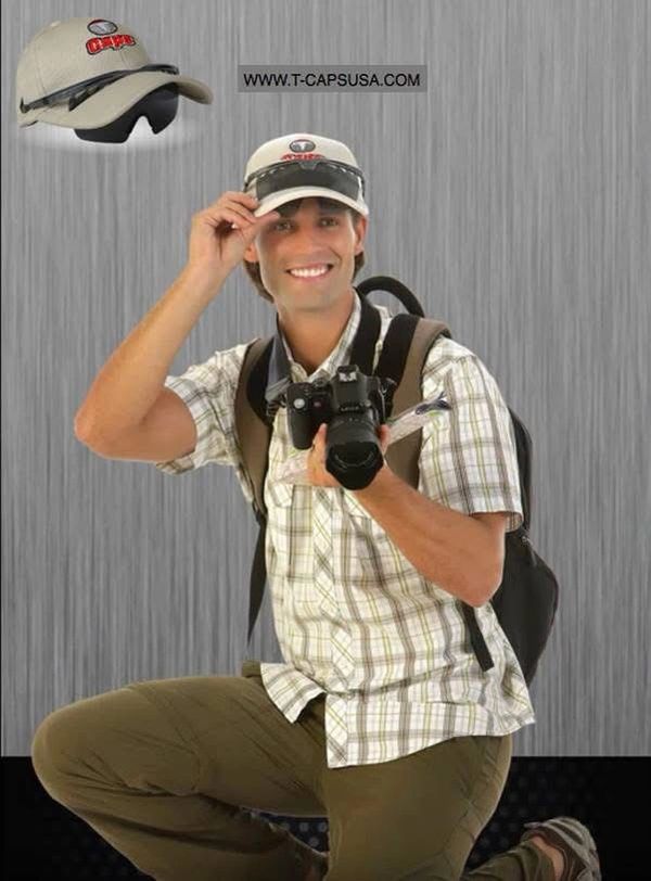 Smiling man with camera wears a promotional cap, posing for a photo.