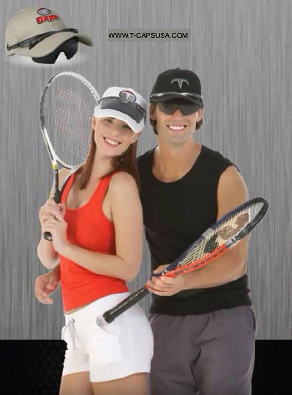 Smiling man and woman in sporty outfits holding tennis rackets and wearing caps.