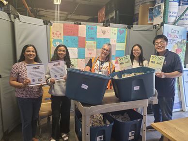 Group of five people holding certificates and standing behind bins filled with items.