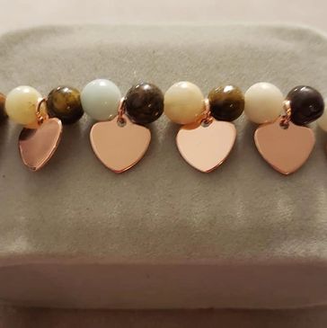 Beaded bracelet with heart-shaped charms on gray cushion.