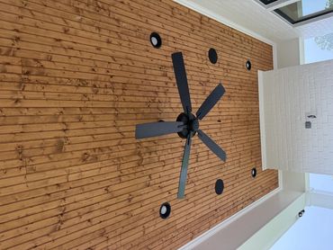 Ceiling fan mounted on wood-paneled ceiling with recessed lights.