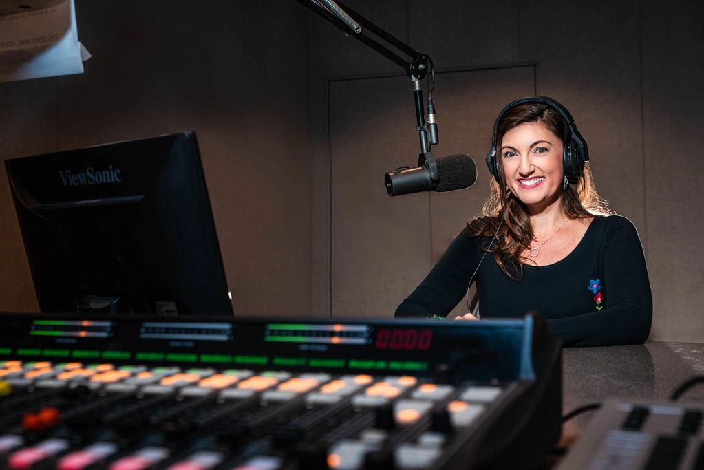 Smiling woman wearing headphones in a radio broadcast studio.