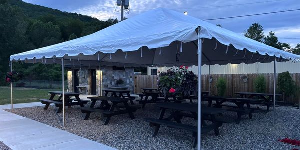 Outdoor picnic area with benches under a large white canopy tent at dusk.