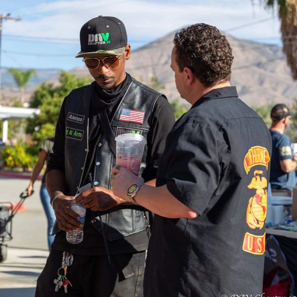 Two men engaged in conversation outdoors, one wearing a leather vest with patches.