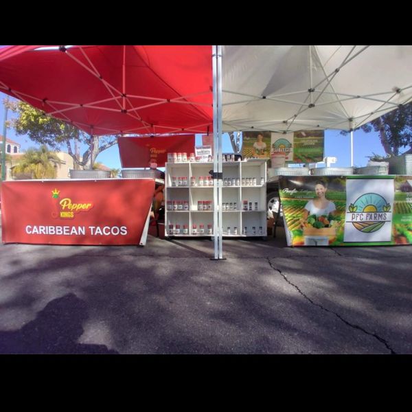 Two market stalls under tents selling Caribbean tacos and farm produce.