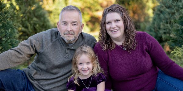 Family portrait of a man, woman, and child outdoors.