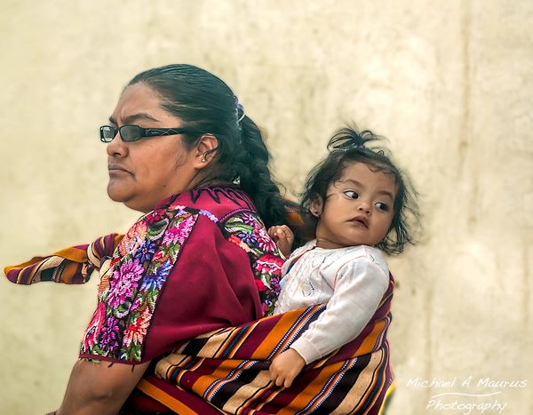 Maya mother with modern sunglasses carrying her baby in a traditional "Rebozo" on her back.