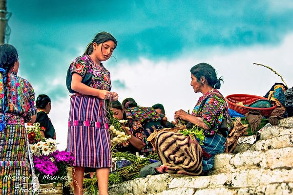 A group of Maya woman and a girls sitting on stairs preparing the flowers for the market.