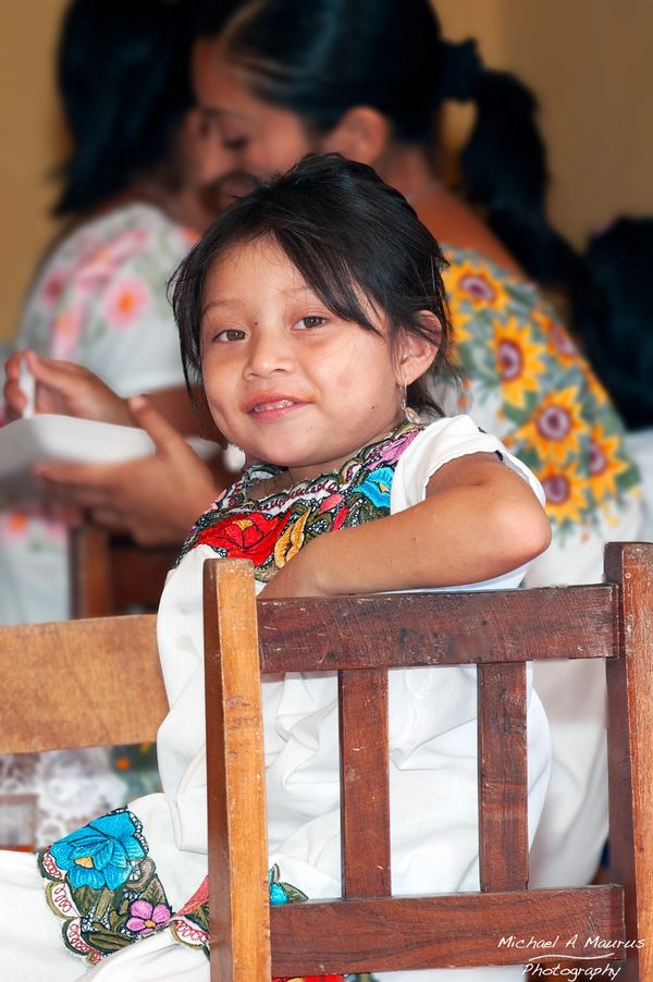 A young Maya girl dressed in the traditional huipil smiling at the camera.