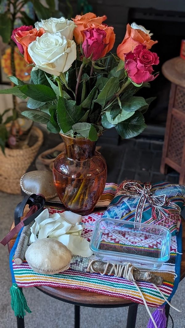 Colorful roses in a brown vase on a decorated table with various objects.