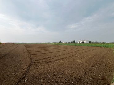 A freshly plowed field under a cloudy sky with distant buildings.