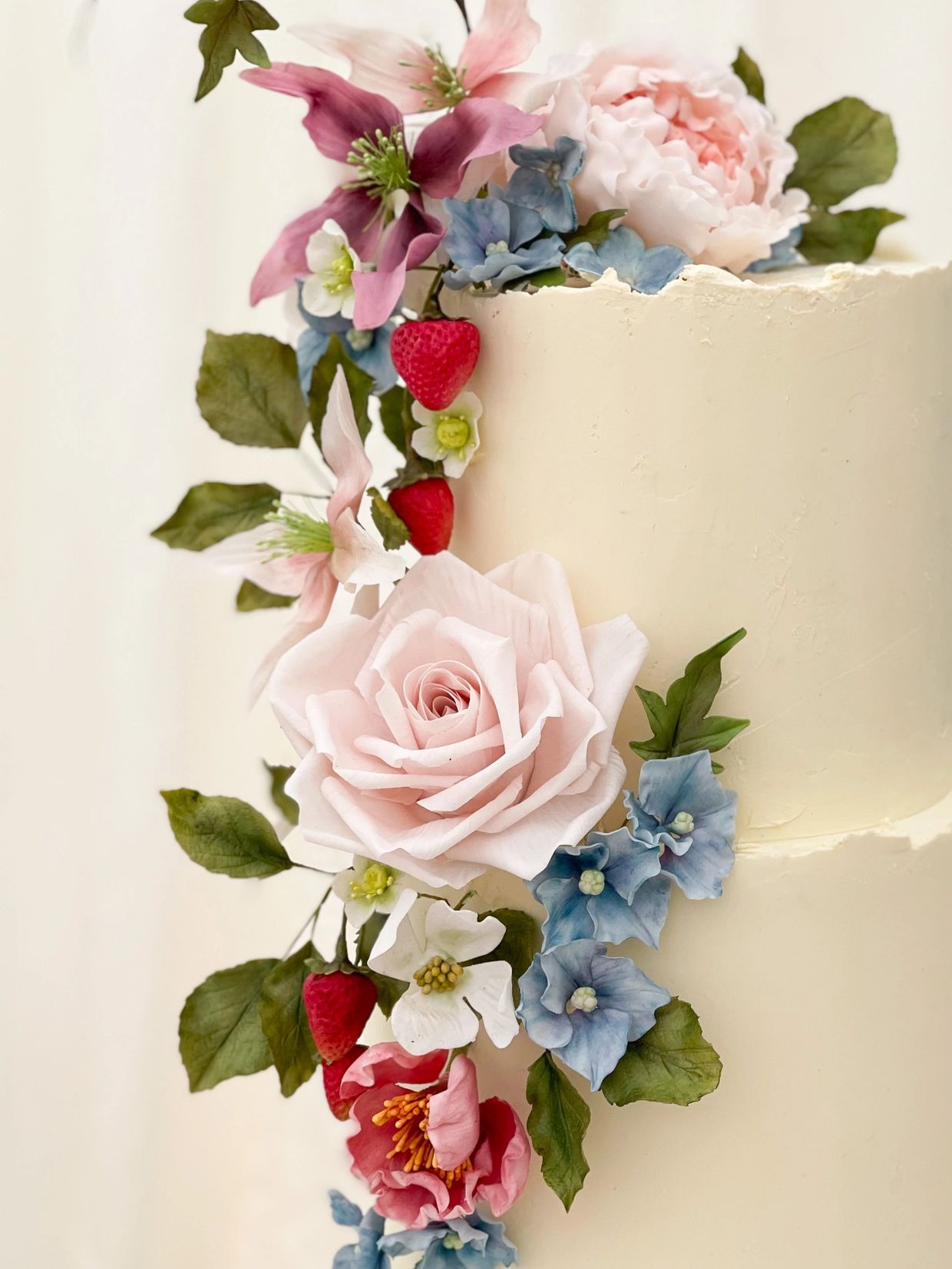 Close up of ganached wedding cake, handmade pale pink sugar rose, sugar strawberries, blue hydrangea