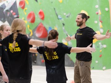 Instructor leads a group in stretching exercises at an indoor climbing gym.