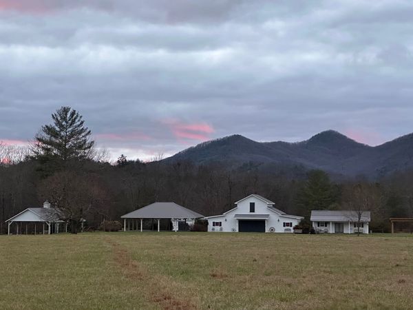 Rural homestead with white buildings against mountain backdrop under cloudy sky.