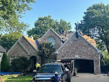 Workers repairing the roof of a brick house on a sunny day.