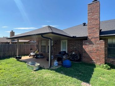 Backyard patio with grill, firewood, and various outdoor items under a covered porch.