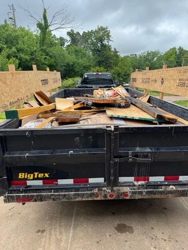A black BigTex trailer loaded with construction debris and wood pieces.