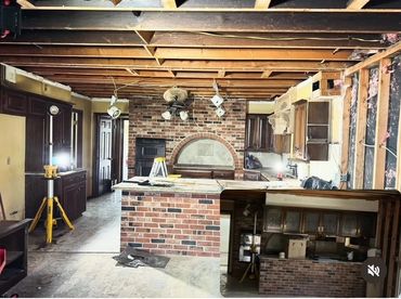 Renovation in progress in a kitchen with exposed ceiling and brick island.