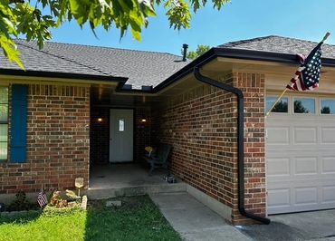 Brick house entrance with an American flag and a green lawn under a clear sky.