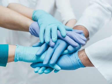 Team of young doctors stacking hands in blue gloves indoor. medical teamwork.