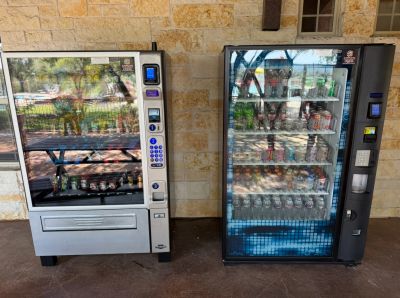 Two vending machines outdoors against a stone wall.