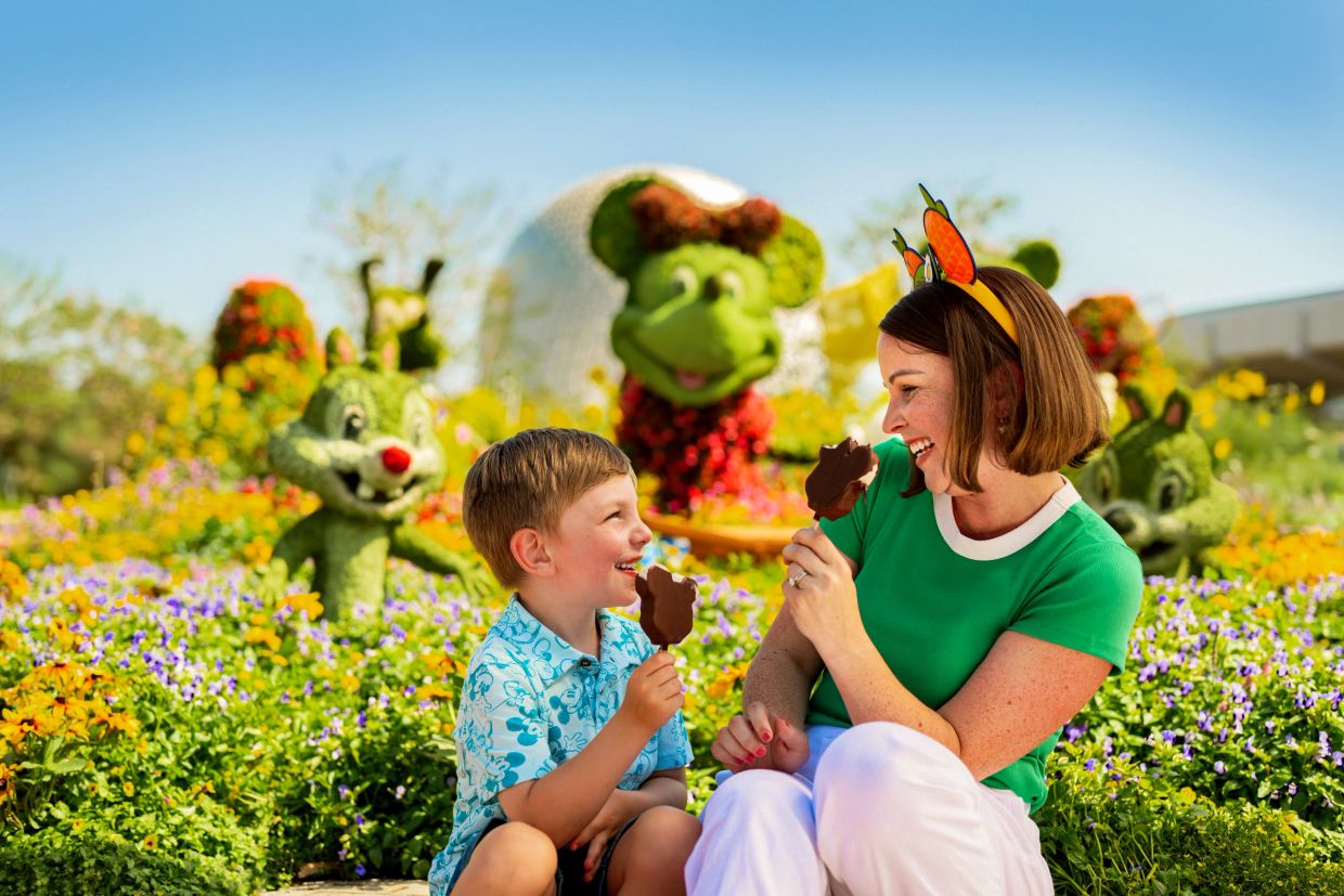 Madre e hijo disfrutando helados en un jardín con figuras de Disney.