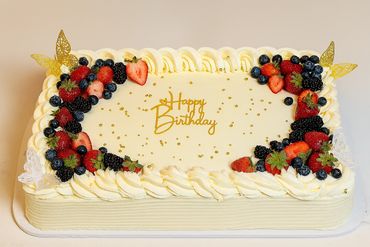 Elegant rectangular birthday cake decorated with fresh berries and gold accents.