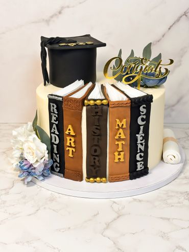 Graduation cake decorated with books, a cap, and Congrats topper.