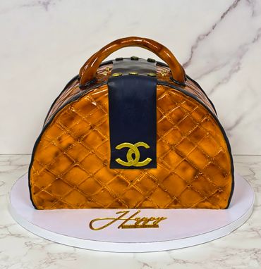 A cake designed to look like a luxurious orange handbag with a black strap and gold logo.
