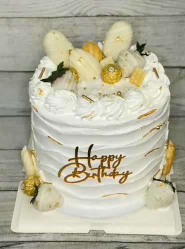 Elegant white birthday cake decorated with gold accents and white chocolate strawberries.