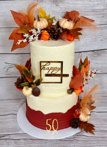 Two-tier autumn-themed birthday cake decorated with pumpkins, leaves, and pinecones.