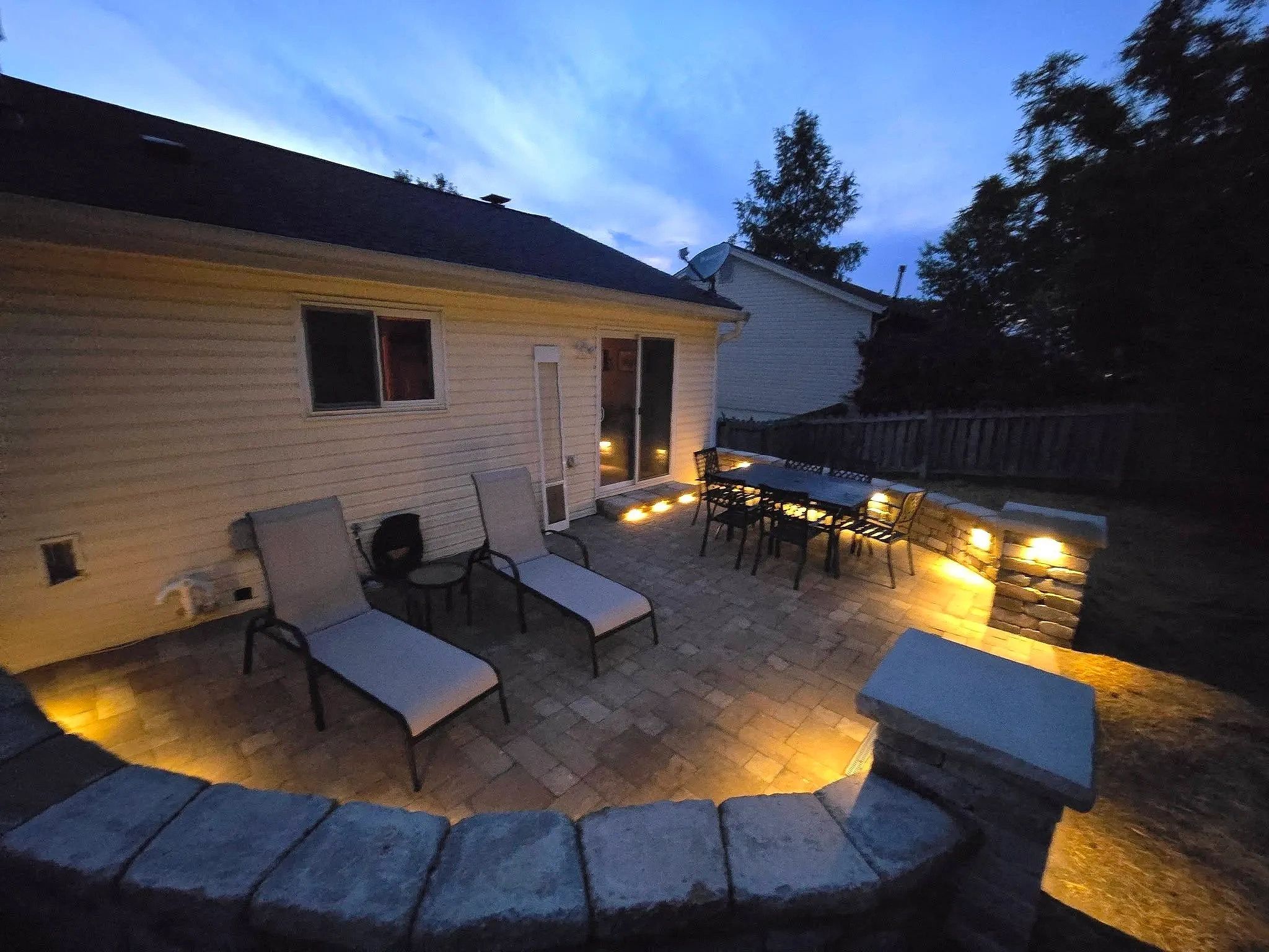 Outdoor patio with lounge chairs and dining table lit at dusk.