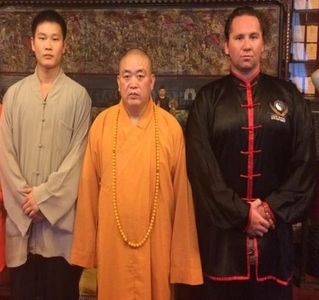 Three men in traditional martial arts attire pose indoors.