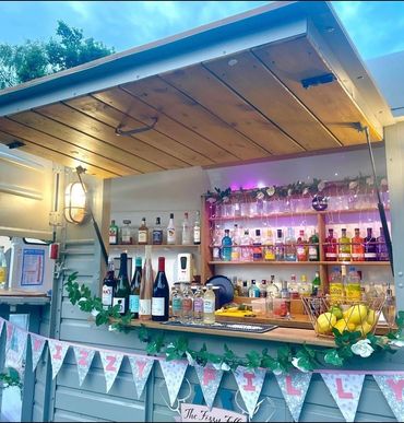 Outdoor mobile bar setup with various spirits and decorative lights.