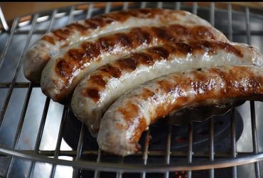 Grilled sausages cooking on a metal grill with char marks.