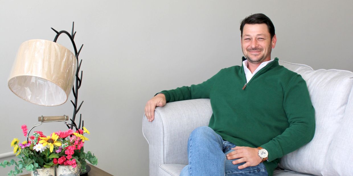 Man in green sweater sitting on a couch, smiling.