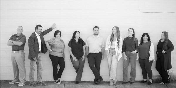 A group of nine people casually posing against a wall outdoors.