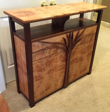 Made from figured maple and black walnut. It has two drawers and two cabinet doors on the front. Par