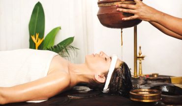 Woman receiving Ayurvedic oil therapy with herbal liquid dripping on forehead.