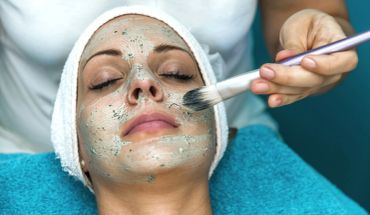 Woman receiving a facial mask treatment with a brush at a spa.