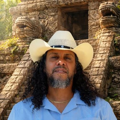Man wearing cowboy hat in front of ancient stone sculpture.
