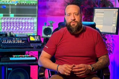 Man with a beard in a recording studio with colorful lights.