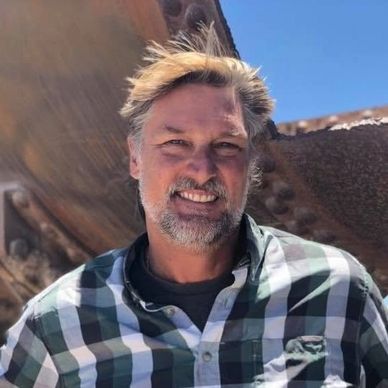 Smiling man with tousled hair outdoors.