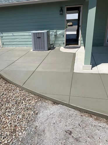 Freshly poured concrete patio addition with a curved countour built around the hvac system