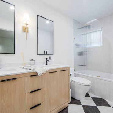 Modern bathroom with dual mirrors, wooden vanity, and patterned tile flooring.